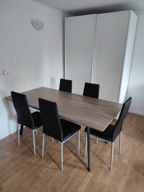 A dining area with a rectangular table, six black chairs, and a white wardrobe in the background.