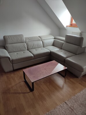 A modern living room with a sectional sofa, a coffee table, and a sloped ceiling with a skylight. - Charming renewed apartment in Rogla (Vitanje)