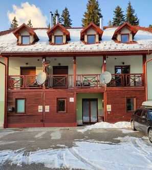 A chalet-style building with multiple dormer windows, a balcony with railings, and a car parked in front. - Charming renewed apartment in Rogla (Vitanje)