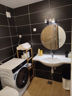 A compact bathroom with a washing machine, a sink, and a mirror.