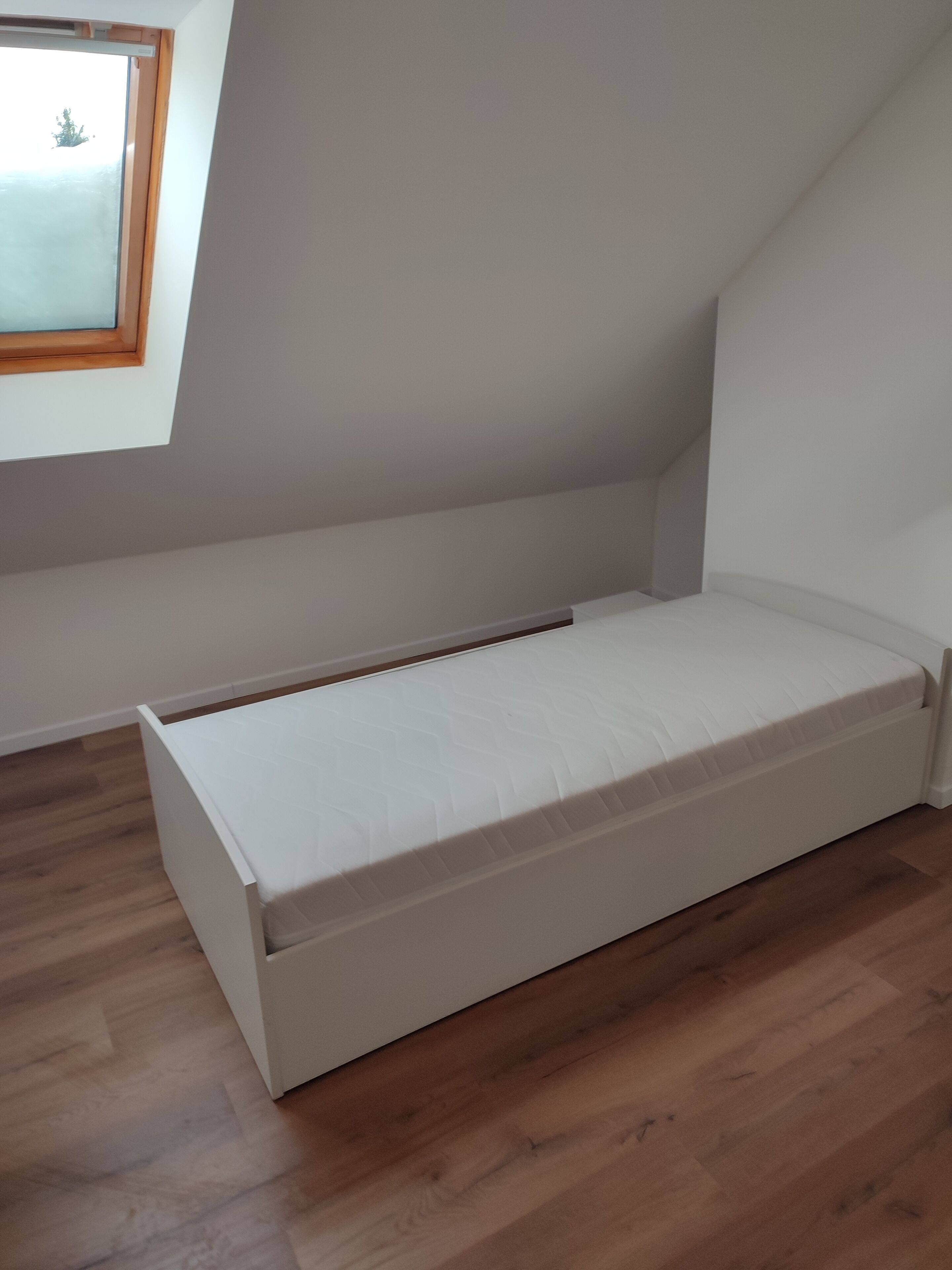 A small, single-bed room with a sloped ceiling and a window.