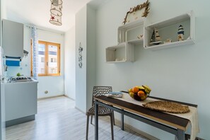 A kitchen with a gas stove, a dining table with a basket of fruit, and a chair. - Mediterranea House A Otranto – 8 Guests, Balcony, Wi-Fi & Air Conditioning (Otranto)