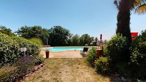 Une piscine entourée d’un jardin, avec une chaise et un palmier.
