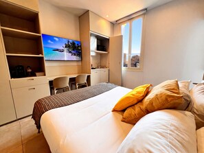 Een hotelkamer met een bed, een bureau, een televisie en een raam met uitzicht op de stad.
