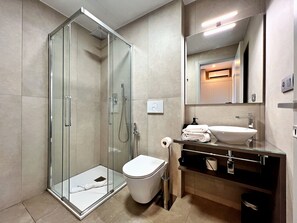 Een moderne badkamer met een douchecabine van glas, een wit toilet, een wastafel met spiegel en een handdoekhouder.