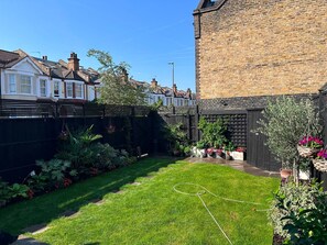 A residential backyard with a lawn, potted plants, and a brick building. - Cosy & Bright  2-Bed House in Earlsfield (London)