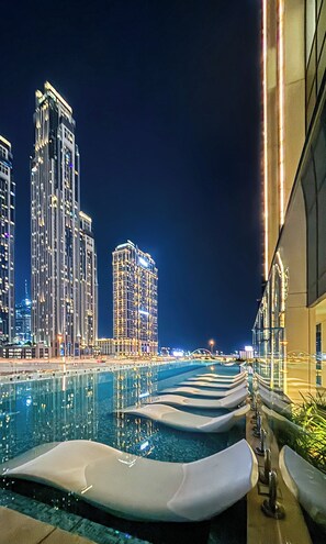 A nighttime view of a pool area with tiered seating and high-rise buildings in the background. - Gala Guests - Urban Oasis Apartments (Dubai)