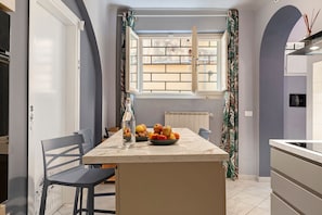 Una cucina con un piano di lavoro in marmo, una ciotola di frutta e una finestra con tende.