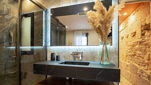 Une salle de bain moderne avec un meuble-lavabo en marbre, une cabine de douche en verre et un mur en pierre rustique.