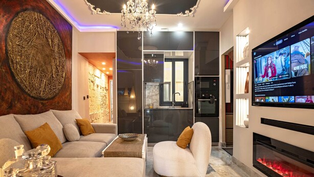 Un salon moderne comprenant un canapé, un fauteuil, un téléviseur, une cheminée et des œuvres d’art décoratives au mur.