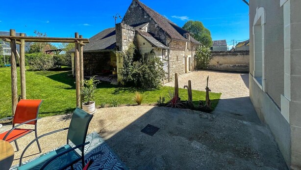 Un bâtiment en pierre doté d’un toit en pente, d’une cour en gravier et d’une pergola en bois.