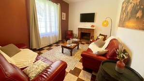 Un salon avec une cheminée, des canapés en cuir, un téléviseur et un sol à carreaux.