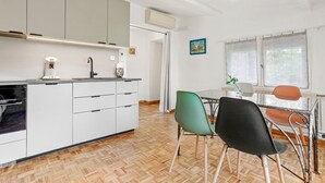 Una cocina moderna con armarios blancos, horno empotrado y comedor con mesa y sillas.