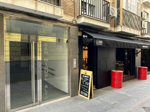 Fachada de loja com paredes de vidro, um letreiro indicando 'SAN MIGUEL ALTA' e uma marquise preta com a inscrição 'TANGO BAR'.