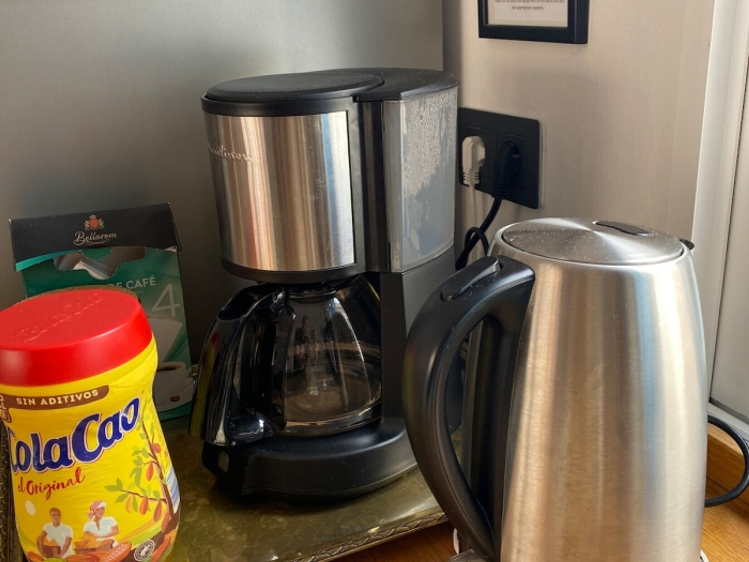 A coffee maker, a kettle, and a can of Coca-Cola on a table.