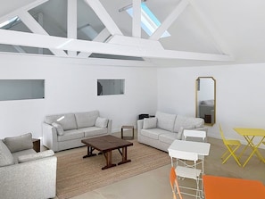 Ein modernes Wohnzimmer mit zwei grauen Sofas, einem Holztisch, einem kleinen weißen Beistelltisch, einem gelben Klapptisch und einem Spiegel an der Wand.
