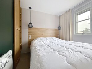 Ein Schlafzimmer mit Holzkopfteil, zwei Pendelleuchten, einem fenster mit Vorhängen und einer Heizung.