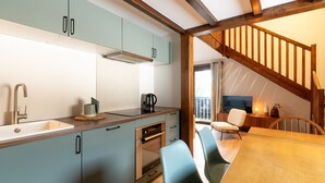 A modern kitchen with light blue cabinets, a wooden dining table, and a staircase leading to a balcony. - Renovated duplex near station - 6 guests (Arâches-la-Frasse)