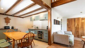 A modern kitchen with wooden beams, a dining area with a wooden table and chairs, and a living room with a sofa. - Renovated duplex near station - 6 guests (Arâches-la-Frasse)