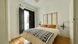 Et soveværelse med seng, natbord, lampe og et vindue med gardiner.