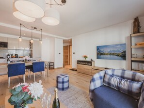 A modern living room with a sofa, a dining area with chairs, a kitchen in the background, and a painting on the wall. - Central apartment - 4 guests (Chamonix-Mont-Blanc)