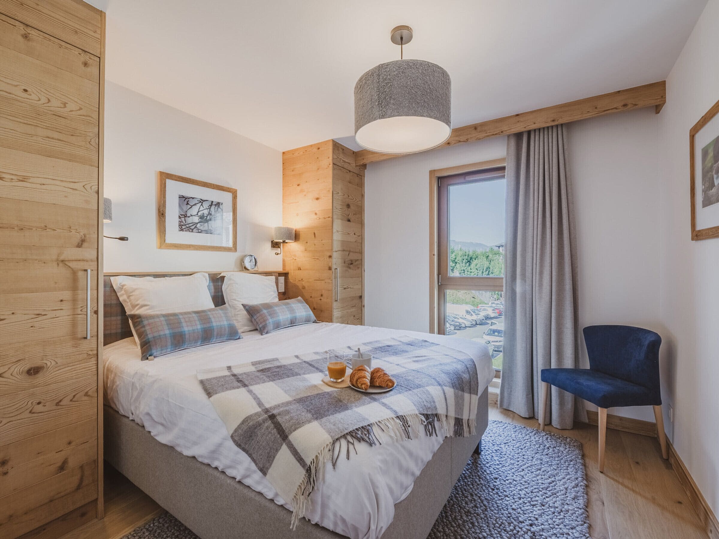 A bedroom with a bed, a chair, a window with a view, and a hanging light fixture.