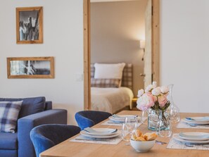 Ein Essbereich mit einem Holztisch, gedeckt für vier Personen, zwei Stühle, einer Blumenvase und einem Bett im Hintergrund.