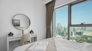 Une chambre d’hôtel comprenant un lit, un bureau, une chaise, un miroir rond et une grande fenêtre donnant sur la ville.