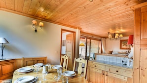 A wooden dining room with a round table set for six, a kitchen with a tiled backsplash, and a wooden ceiling. - Spacious apartment near slopes - 6 guests (Les Gets)