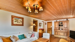 A cozy living room with a wooden ceiling, a sofa with patterned cushions, a wooden coffee table, and a yellow armchair. - Spacious apartment near slopes - 6 guests (Les Gets)