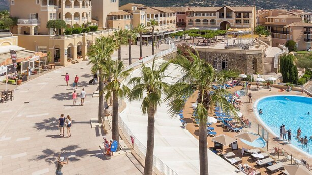 Een resort met een zwembad, palmbomen en een bergachtig achtergrond.