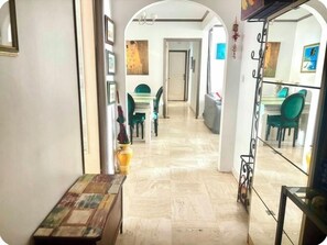 A hallway leading to a dining area with green chairs and a table, a vase with an umbrella, and a mirror reflecting the room. - At the gates of Cannes: Apartment 100m2 and terrace, center, Croisette on foot (Le Cannet)