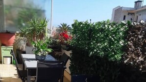 Eine Terrassengruppe mit Tisch und Stühlen, umgeben von Blumentöpfen und einem Hecken.