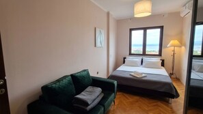 Ein Schlafzimmer mit einem Bett, einem grünen Sofa, einem Fenster mit Blick und einer Stehlampe.