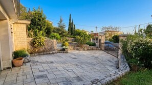 Eine gepflasterte Terrasse mit Steinmauern, einem Metallgitter und verschiedenen Pflanzen.