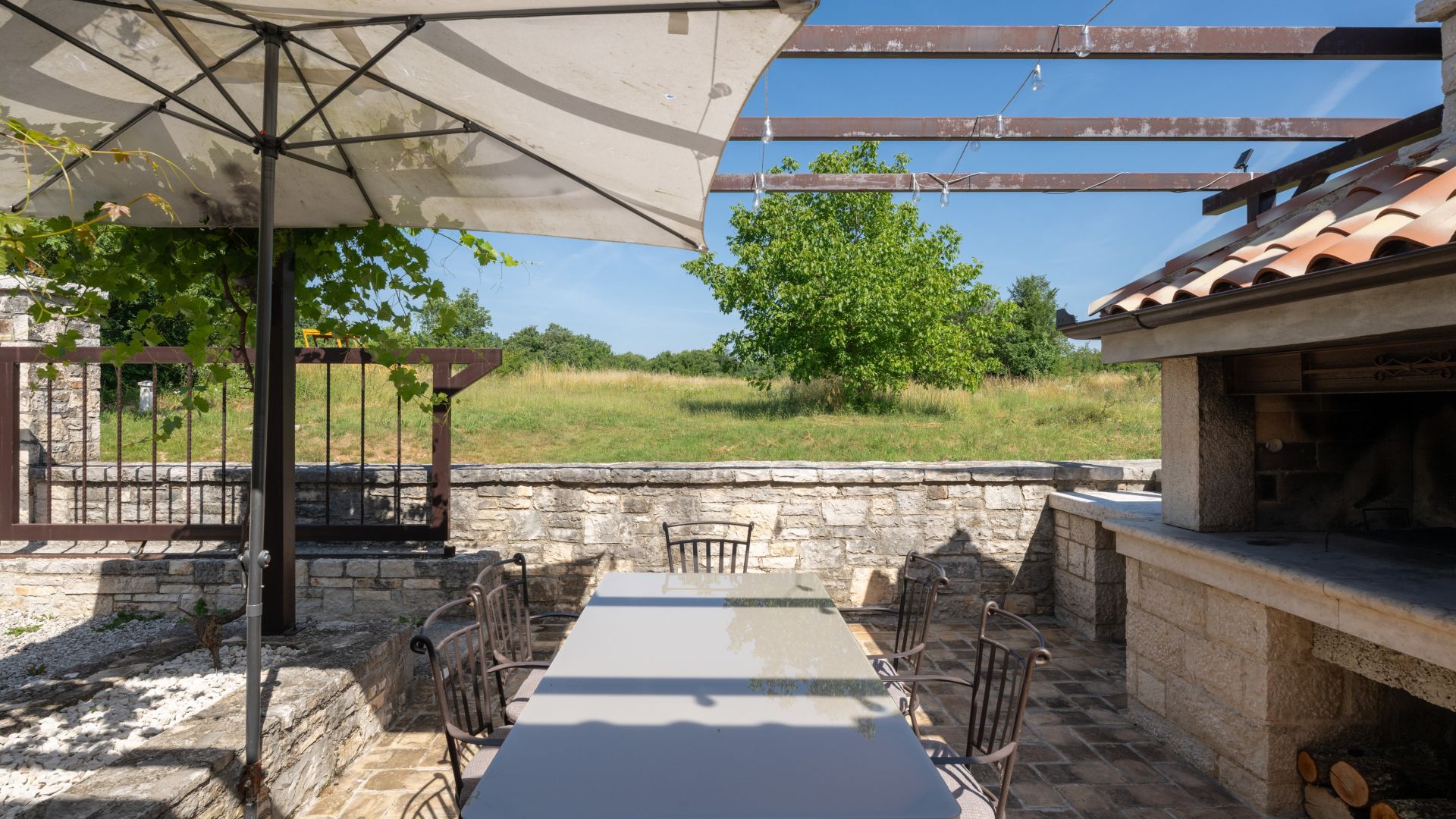An outdoor patio with a table and chairs, a pergola with a canopy, and a stone wall.