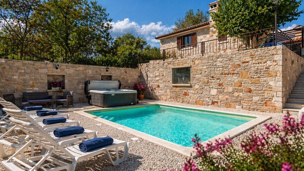 Un espace piscine entouré de murs en pierre, avec des chaises longues et un jacuzzi.