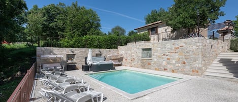 A swimming pool with lounge chairs, a hot tub, and a stone wall.