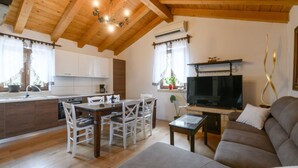 Une cuisine moderne avec des meubles blancs, une table à manger avec des chaises, un téléviseur et un canapé.