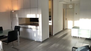 A modern kitchen with white cabinets, a black countertop, and a dining area with a glass table and chairs.