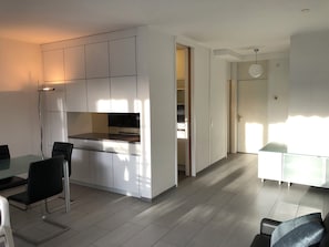 A modern kitchen with white cabinets, a black countertop, and a dining area with a glass table and chairs. - Apartment in the park (Minusio)