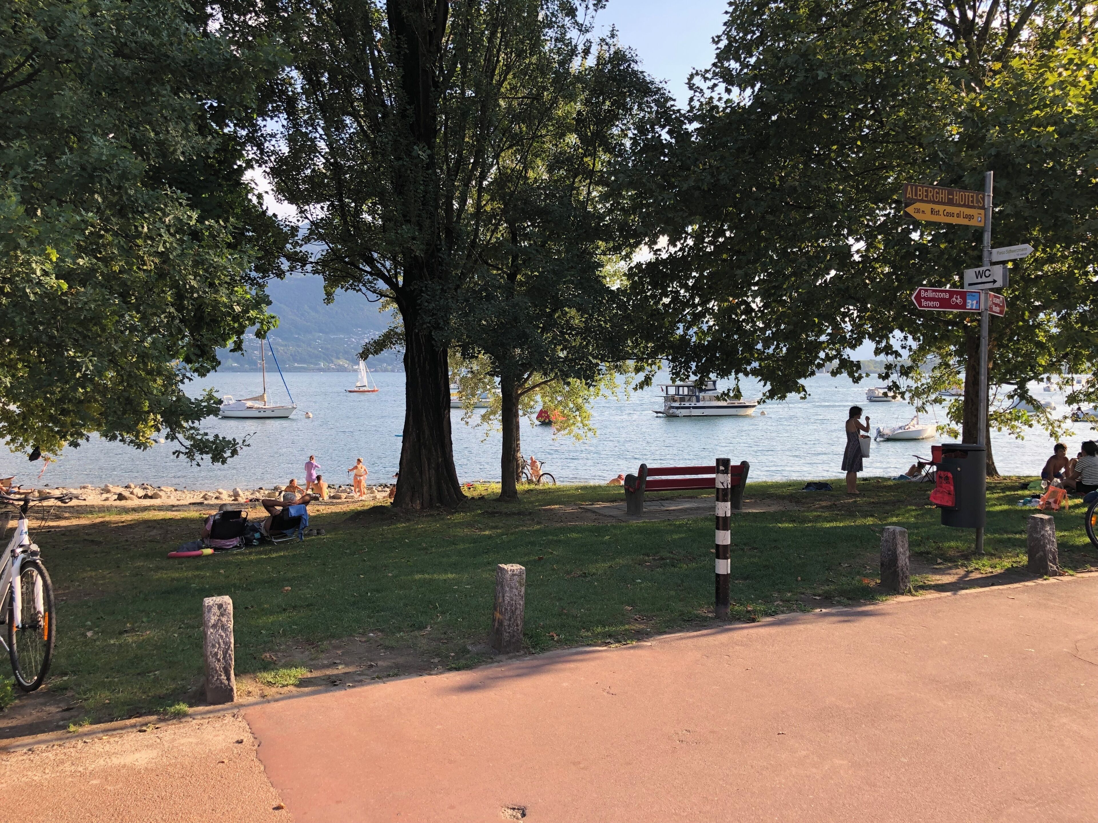 En park ved søen med en bænk, en cykel og et skilt med vejvisning.