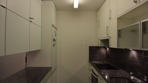 A compact kitchen with white cabinets, a granite countertop, and a stainless steel sink.