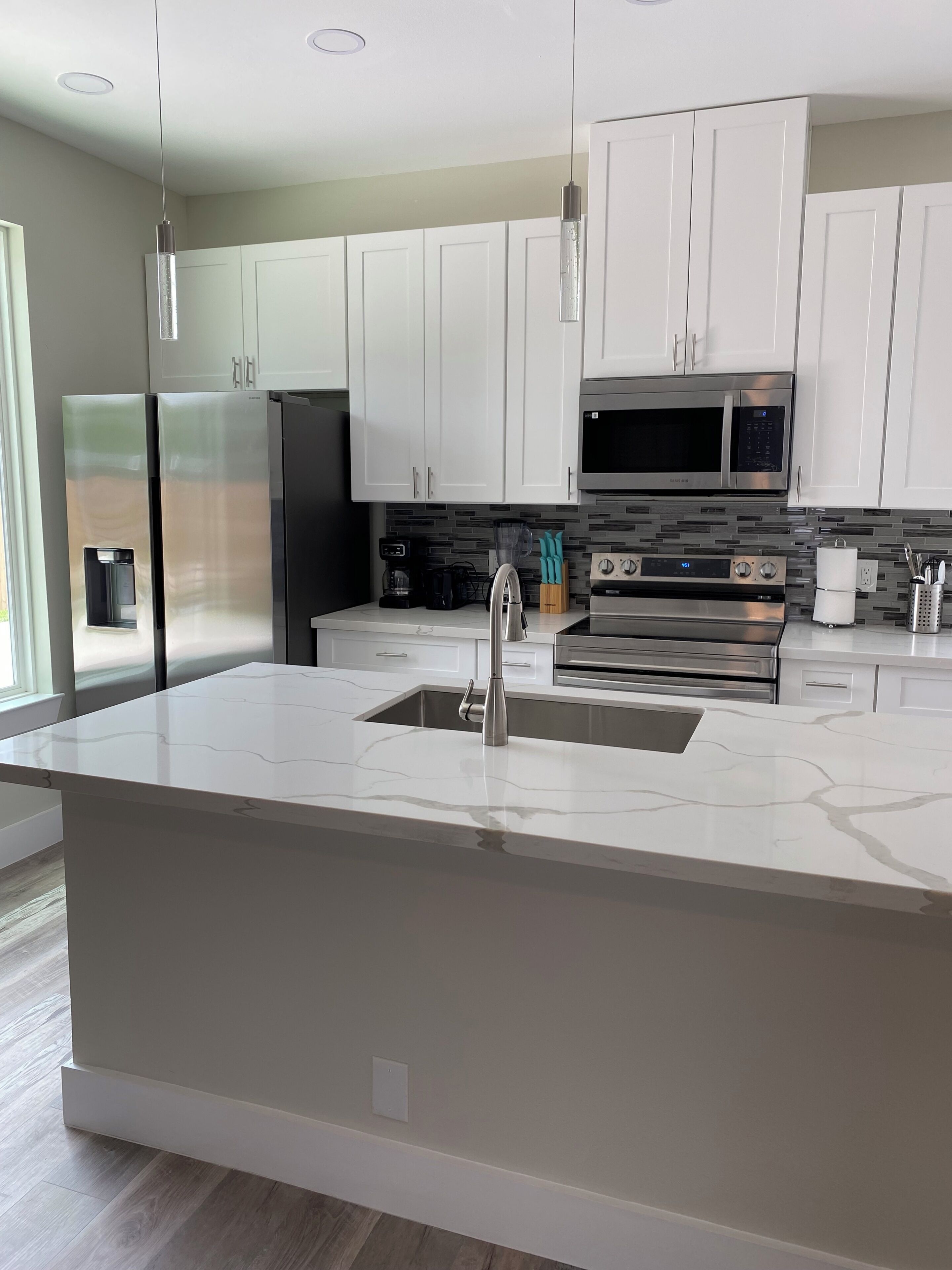 A modern kitchen with white cabinets, stainless steel appliances, a marble countertop, and a built-in sink.