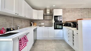 Una cocina moderna con armarios blancos, una campana extractora de acero inoxidable, un horno empotrado y una cafetera.