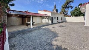 Un edificio con un espacio exterior techado, una mesa pequeña y un camino de entrada de grava.