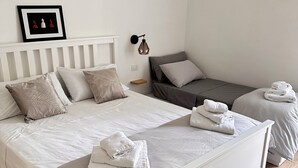 A bedroom with a large bed, a smaller bed, a bedside table, a wall-mounted lamp, and a framed picture on the wall. - Donna Flora's House (Napoli)