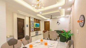 A dining area with a marble table, chairs, and a television in the background. - Tucson 2BHK Forest view by Homeyhuts (Dehradun)