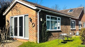 Une maison de plain-pied en briques, avec un toit en tuiles, de grandes fenêtres et un petit jardin où poussent des jonquilles.