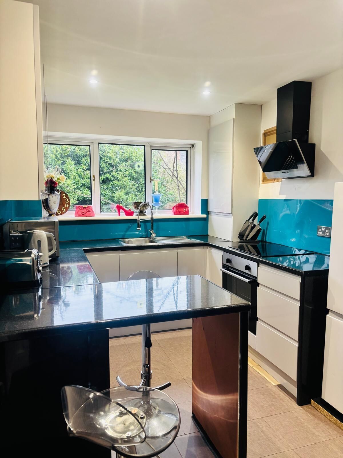 Uma cozinha moderna com ilha central, janela com vista para o verde e exaustor preto.